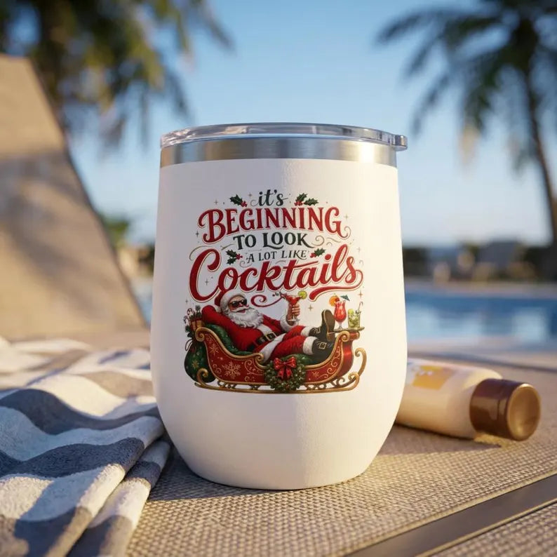 White stemless tumbler with a clear lid, Santa in a sleigh, and It's Beginning to Look a Lot Like Cocktails lettering.