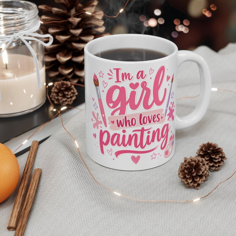 White handled mug with pink I’m a Girl Who Loves Painting lettering, paintbrushes, hearts, stars, and paint splashes.