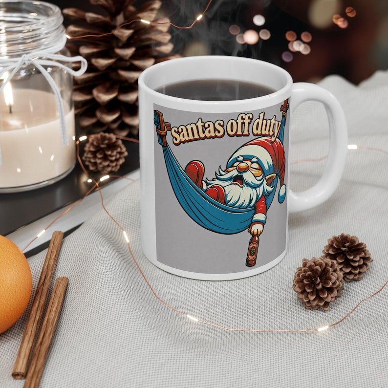 White handled mug featuring Santa relaxing in a blue hammock with a bottle and Santa’s Off Duty lettering.