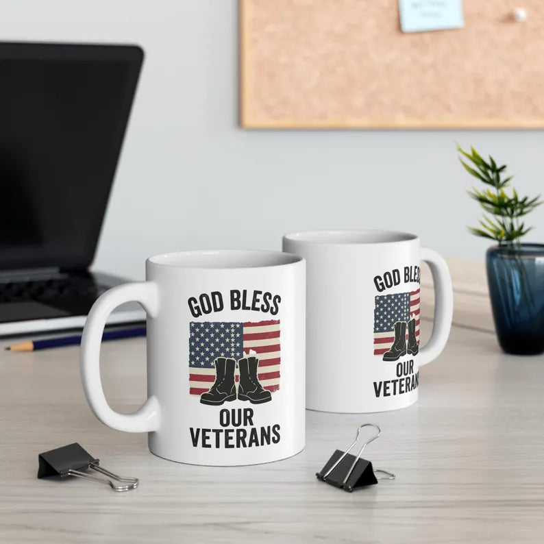 Two white handled mugs displaying God Bless Our Veterans lettering, an American flag, and boots. Listing includes one mug.